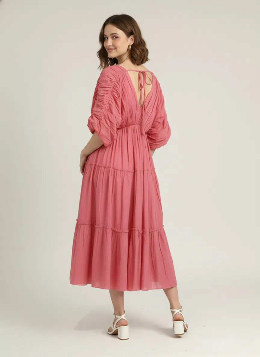 Back view of a woman wearing a dusty rose pink pure cotton tiered midi dress, showcasing the V-back with a delicate tie detail, against a plain white background.