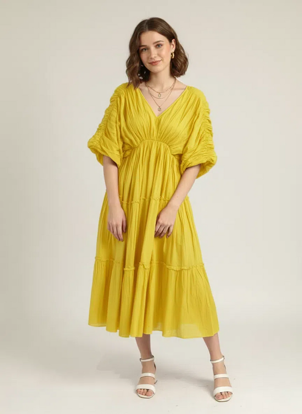 Front view of a woman standing, smiling softly, wearing a luminous lemon yellow pure cotton tiered midi dress with a V-neck and ruched short sleeves, against a plain white background.
