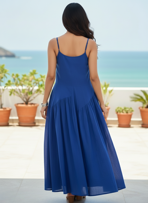 Back view of woman in royal sapphire blue flowy maxi dress, showing plain back and panelled skirt, overlooking the sea
