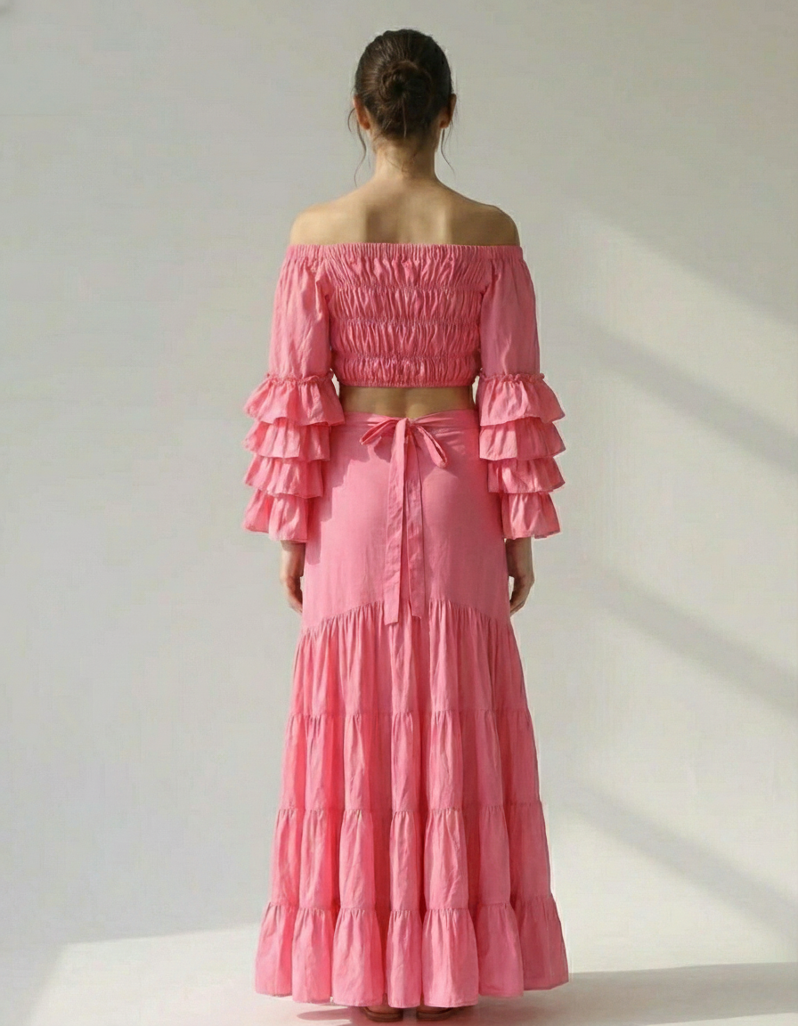 Back view of the pink ensemble showing the smocked elastic back of the crop top and the bow tie closure of the wrap skirt.