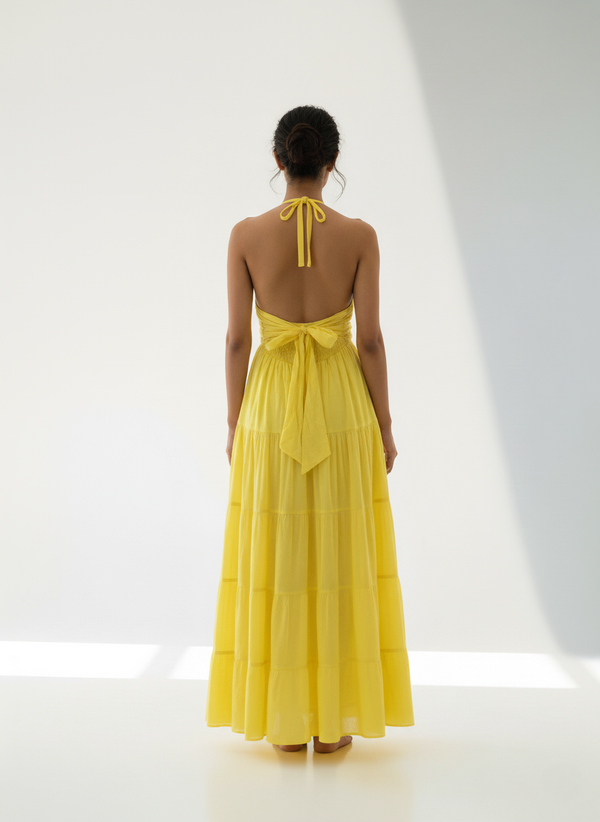 Back view of woman in sunbeam yellow halter tiered maxi dress, showing halter tie and open back