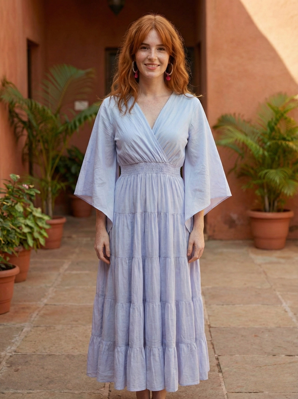 Woman in a light lavender kimono style maxi dress standing in front of a building with plants.