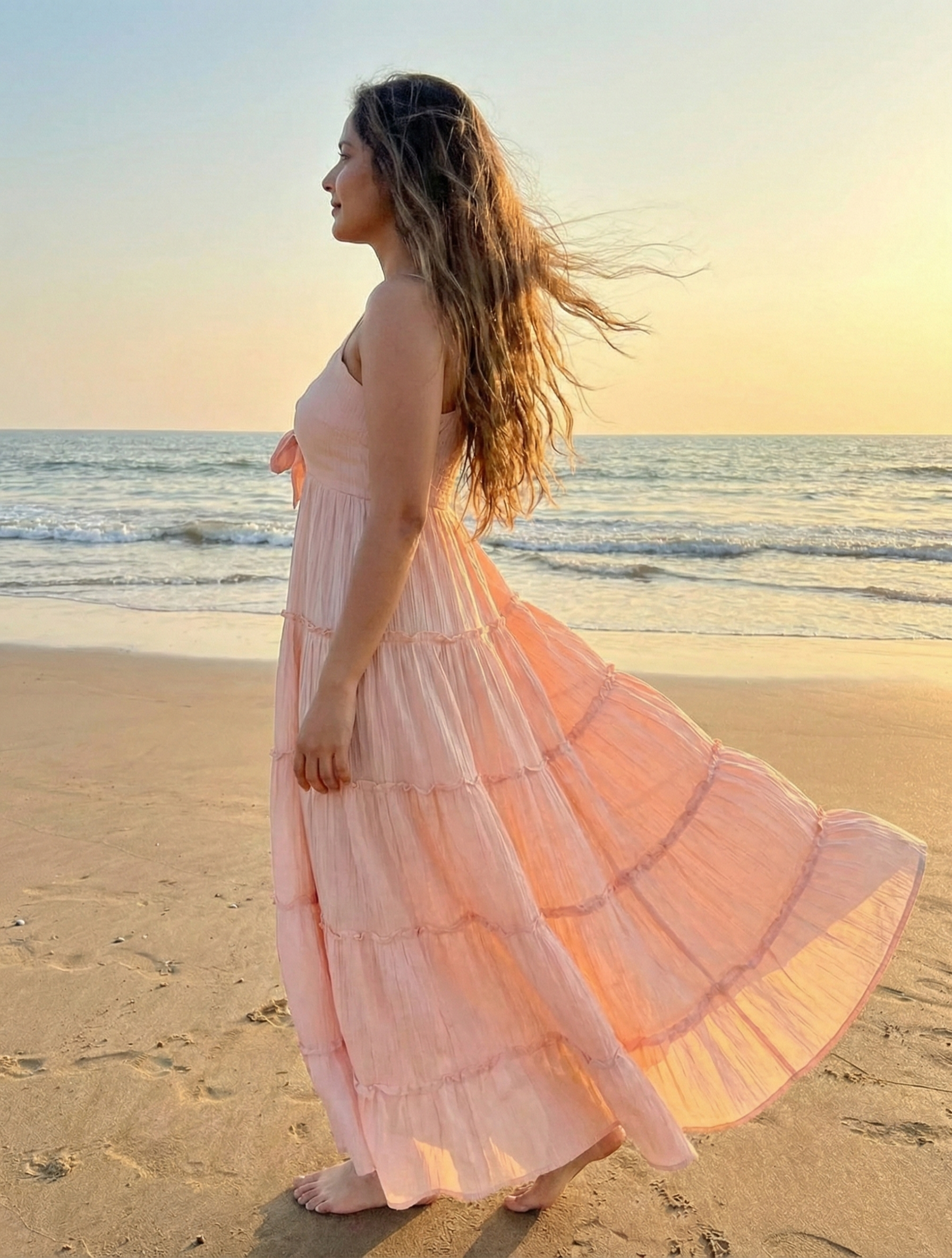Woman in a Peach long dress standing on a beach at sunset