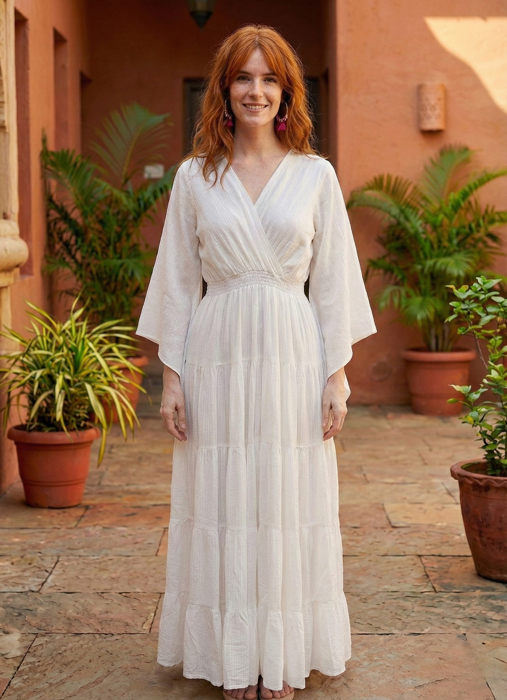 Woman in a white dress standing in front of a building with plants.