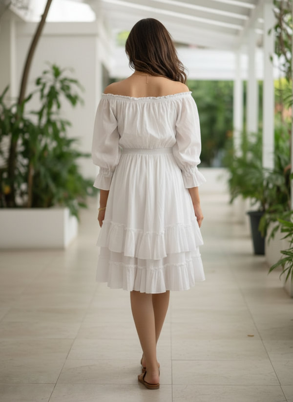 Back view of a woman walking away down a tiled hallway, wearing a white off-shoulder tiered pure cotton midi dress, surrounded by lush green plants.