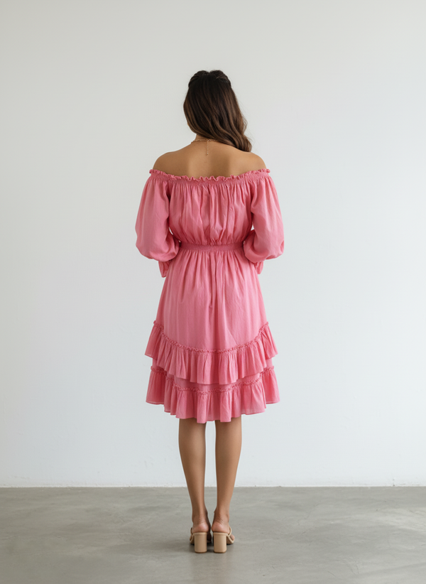 Back view of a woman wearing a radiant pink pure cotton off-shoulder tiered mini dress. The dress has long sleeves and an elasticated waist, set against a plain white background.